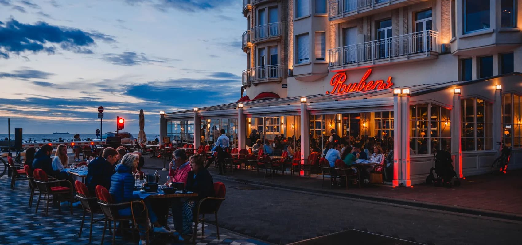 Terrasse de restaurant remplie de clients en bord de mer à la tombée du jour