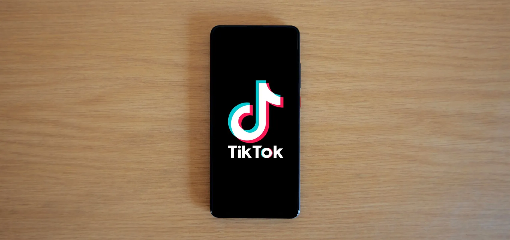 Smartphone affichant le logo TikTok, posé sur un plan de travail en bois