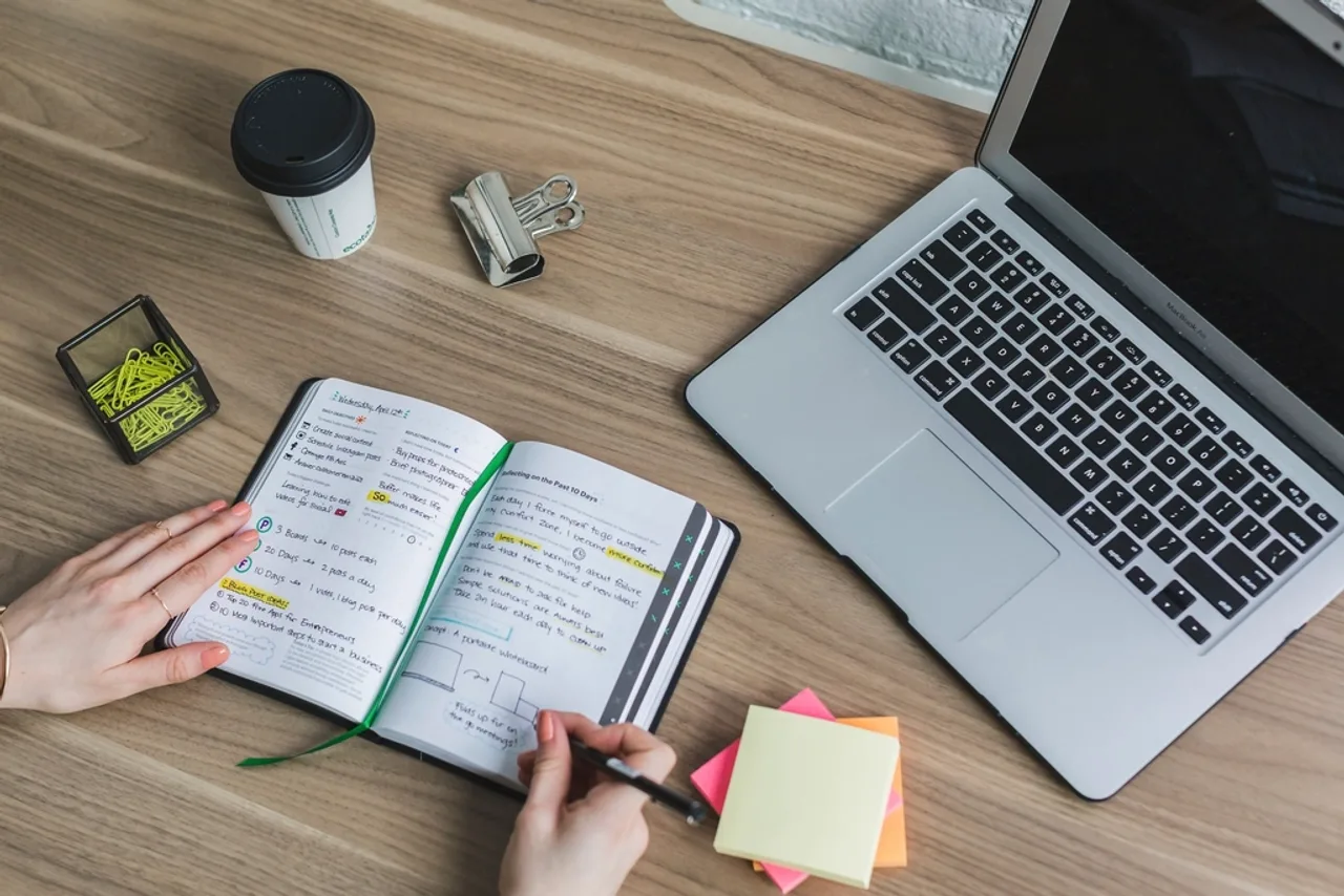 Mains prenant des notes dans un carnet de planification à côté d’un ordinateur portable et de post-it