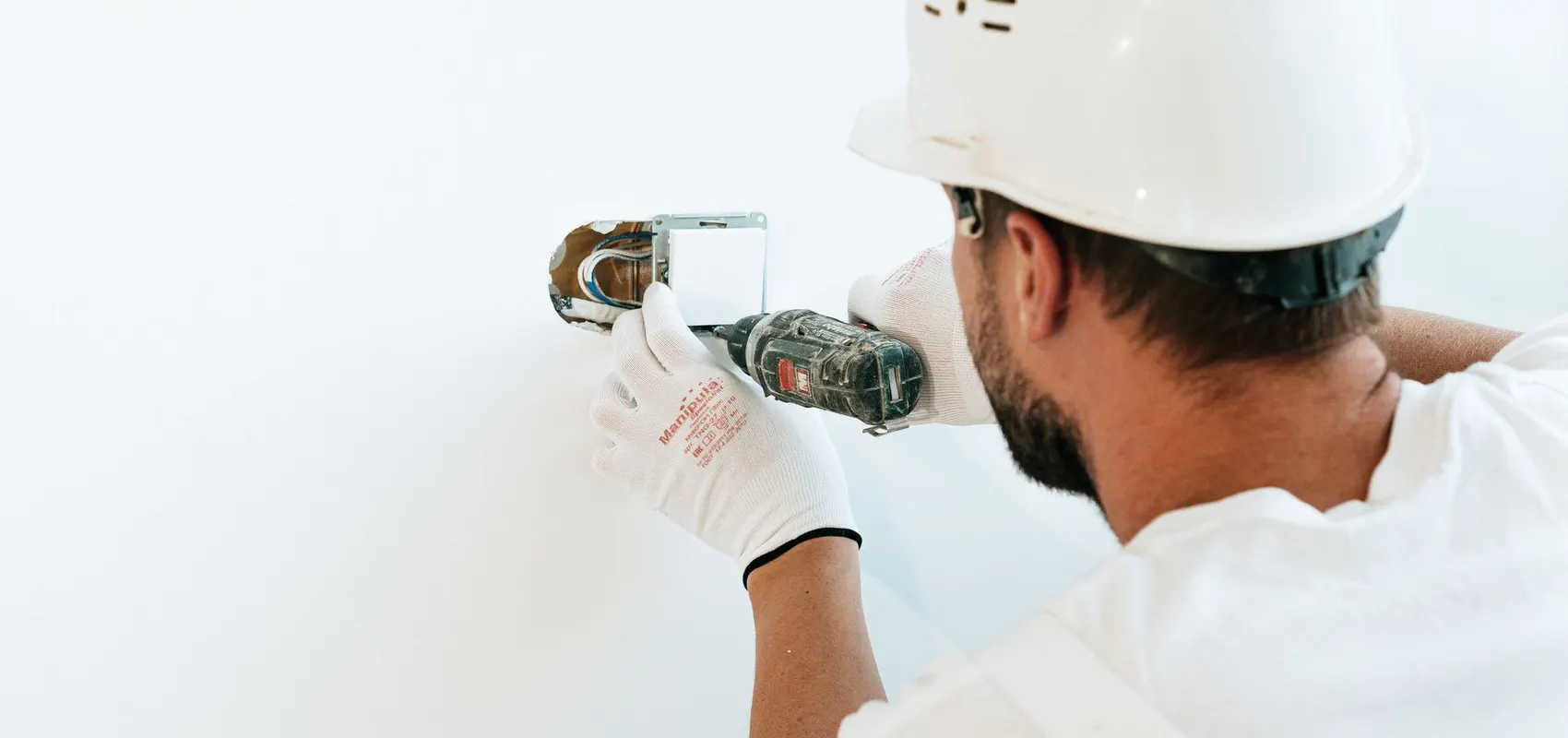 Électricien en casque de chantier qui fixe une boîte d’encastrement au mur avec une visseuse