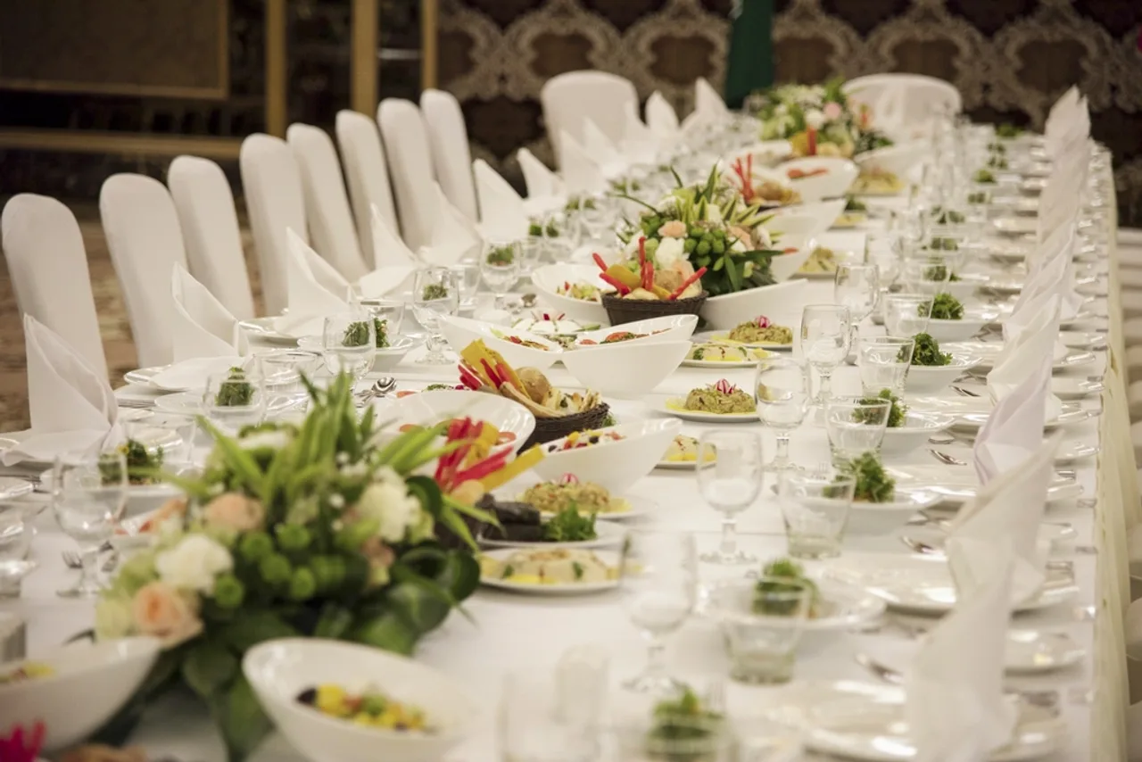 Longue table de banquet dressée de blanc avec fleurs et assiettes garnies